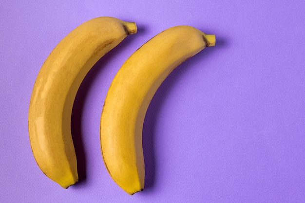Stile minimalista Il modello della frutta con la banana matura gialla fruttifica sopra fondo porpora.