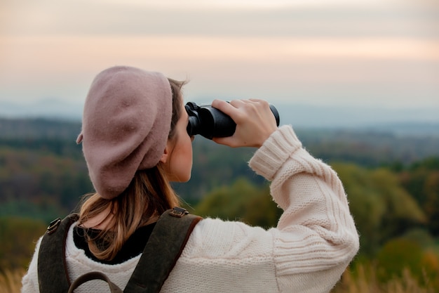 Stile ragazza con binocolo e zaino in campagna con montagne sullo sfondo