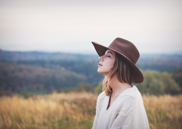 Stile ragazza in maglione e cappello in campagna con montagne sullo sfondo