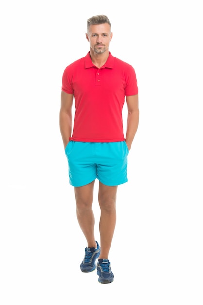 Stile sportivo. Abbigliamento maschile e alla moda. Fronte calmo dell'uomo che posa con confidenza il fondo bianco. L'uomo sembra bello in maglietta e pantaloncini. Vestito sportivo da ragazzo. Concetto di moda. Negozio di abbigliamento modello uomo.