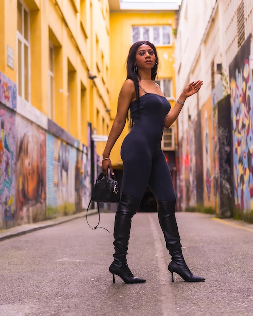 Stile urbano di una ragazza nera alla moda in abito nero e stivali alti