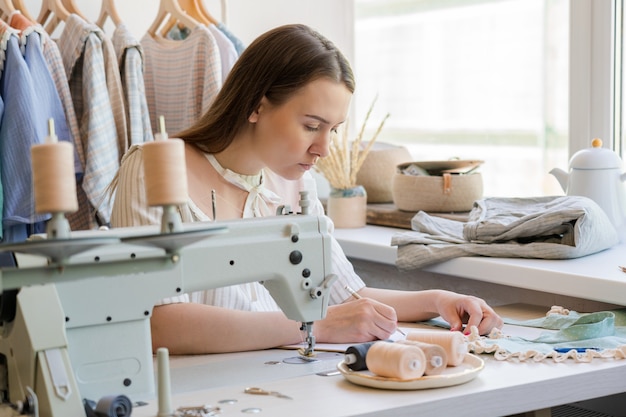 Stilista che disegna vestiti disegna mentre è seduto al suo posto di lavoro con una macchina da cucire