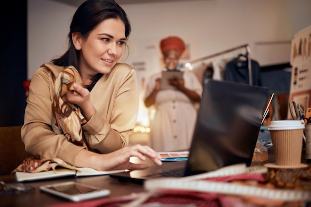 Stilista di moda donna e laptop che pianificano idee di tessuto e tecnologia internet in studio tessile Felice computer su misura o produzione con team in avvio di piccole imprese o laboratorio creativo