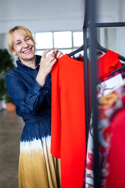 Stilista professionista della donna bionda di risata dell'acquirente che sceglie i vestiti alla boutique di moda