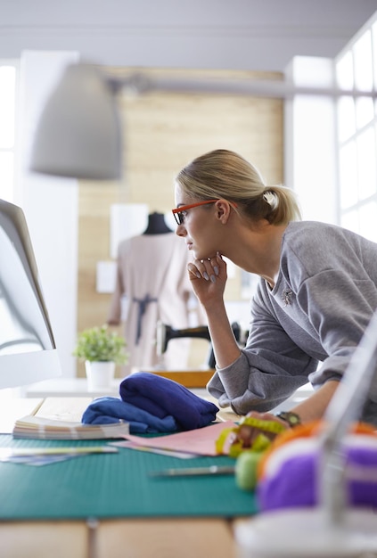 Stilisti di moda giovani femmine attraenti che si appoggiano sulla scrivania dell'ufficio che lavora con un computer portatile