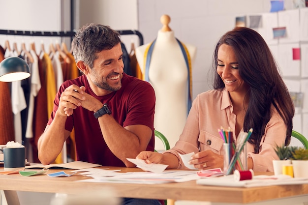 Stilisti di moda maschili e femminili in studio che lavorano su schizzi e disegni alla scrivania