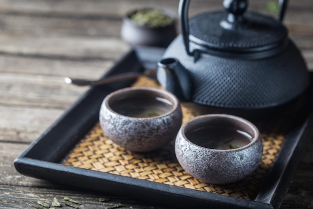 Still-life di sano tè verde giapponese in piccole tazze e teiera su sfondo scuro