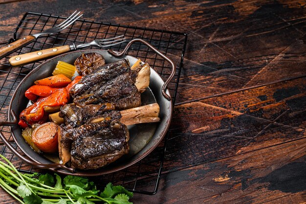Stinco di agnello brasato fatto in casa con salsa ed erbe aromatiche in un vassoio d'acciaio Sfondo in legno Vista dall'alto Spazio di copia