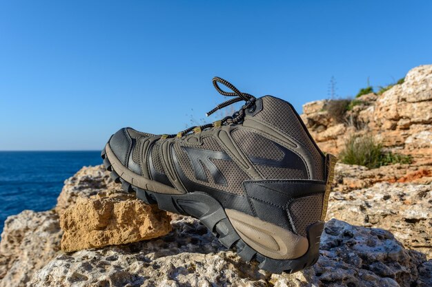 Stivali da trekking verde oliva su uno sfondo naturale di mare e rocce