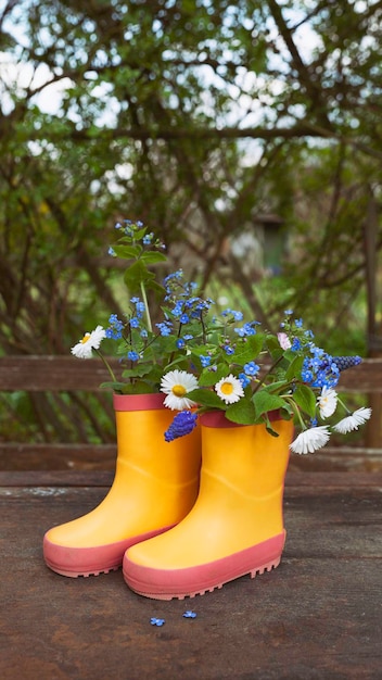 Stivali di gomma gialli con bouquet di fiori primaverili su fondo di legno rurale grezzo Sfondo naturale
