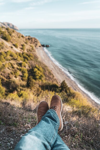 Stivali e gambe da uomo con la costa sullo sfondo. Concetto di esplorazione e avventure