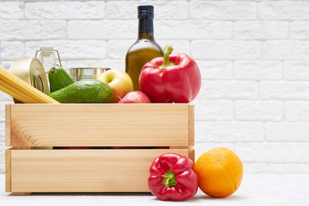 Stock alimentari in una scatola di legno. Verdure, olio, frutta, cibo in scatola, pasta. Donazione, consegna di cibo, coronavirus