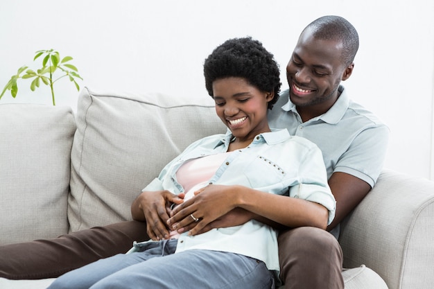 Stomaco della donna incinta commovente dell'uomo sul sofà a casa