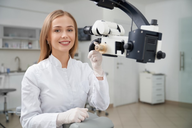 Stomatologo che posa in odontoiatria vicino al microscopio dentale.