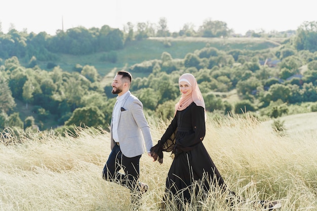 Storia d'amore musulmana di una coppia mista. L'uomo e la donna sorridono e camminano sulle verdi colline.