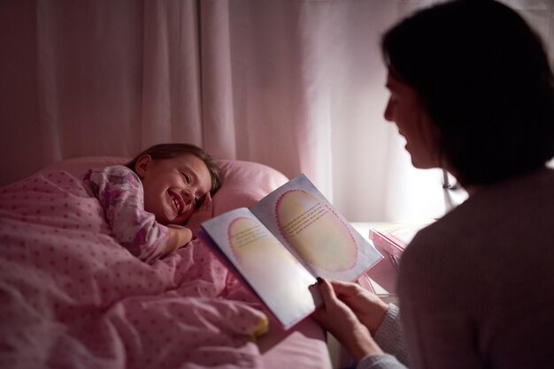 Storie per accendere i suoi sogni d'oro Inquadratura ritagliata di una bambina sdraiata a letto mentre sua madre legge una favola della buonanotte