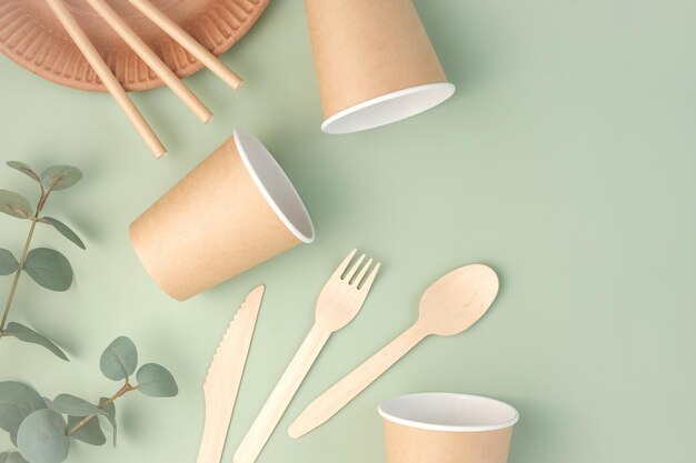 Stoviglie ecologiche su sfondo verde Vista dall'alto Senza plastica Set di utensili in carta marrone Cibo di strada Imballaggi riciclabili Zero sprechi Articoli per la carta Mockup usa e getta Tazza da asporto Posate in legno