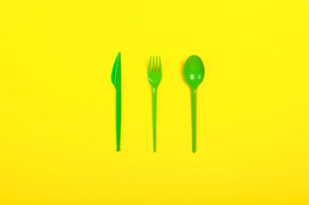 Stoviglie ed apparecchi di plastica eliminabili verdi per l'alimento su un fondo giallo. Forchetta, cucchiaio e coltello. Concetto di plastica, nocivo, inquinamento ambientale, fermare la plastica. Vista piana, vista dall'alto.