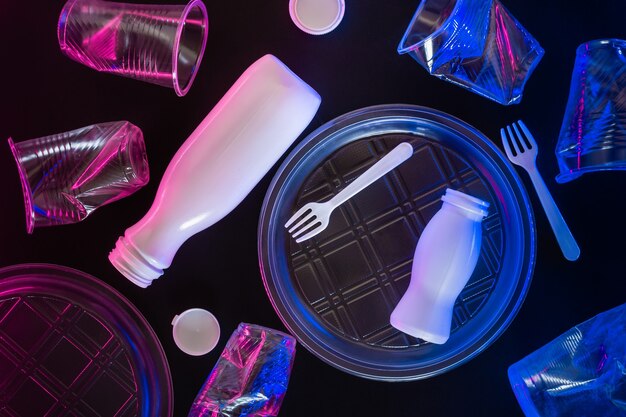 Stoviglie in plastica trasparente con illuminazione al neon su sfondo nero. Concetto di inquinamento ambientale