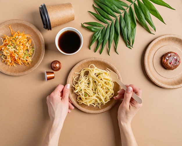 Stoviglie monouso eco friendly zero rifiuti con pasta, insalata e ciambella vista dall'alto piatto giaceva su sfondo marrone