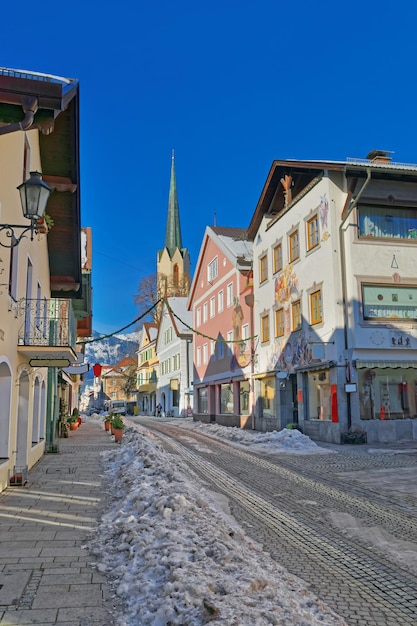 Strada accogliente con case dipinte con cura e chiesa Maria-Himmelfahrt (giorno dell'Assunzione) a Garmisch-Partenkirchen. È una località di villeggiatura di montagna in Baviera, nella Germania meridionale, nel cuore delle Alpi