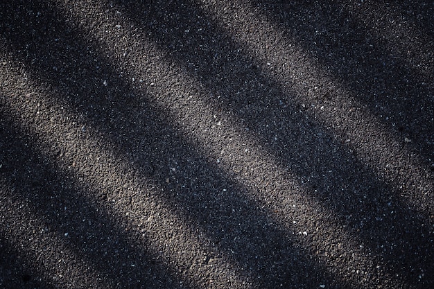 Strada asfaltata con un'ombra scura della recinzione. Le strisce astratte sono chiare e scure.