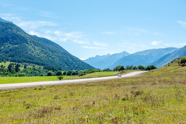 Strada asfaltata e campi verdi con montagne sotto il cielo blu