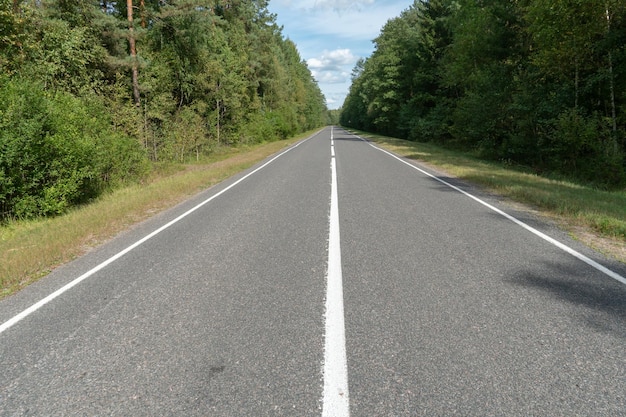 Strada asfaltata vuota attraverso boschi e campi Nuova pavimentazione in asfalto fresco lontano dalla città Sviluppo di infrastrutture rurali Le linee di segnaletica stradale si chiudono