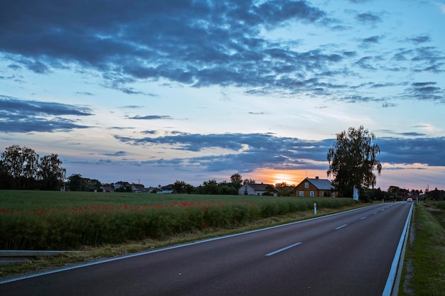 Strada attraverso l'Europa sullo sfondo di un bellissimo cielo al tramonto, un paesaggio e un campo di papaveri