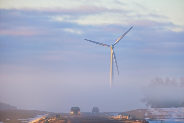 Strada con auto in movimento verso centrali eoliche semi nascoste nella nebbia All'inizio dell'alba in inverno Concetto di energia rinnovabile