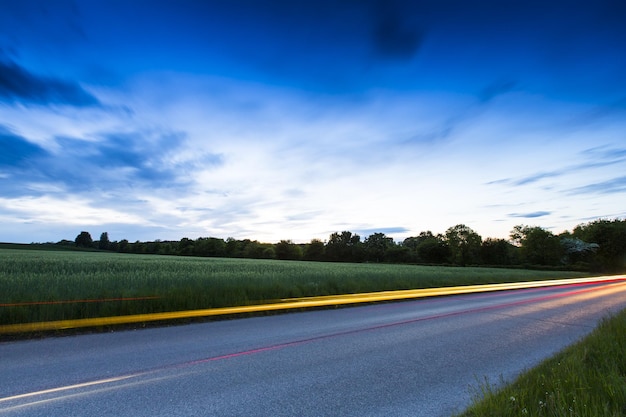 Strada di campagna con strisce luminose per auto al tramonto