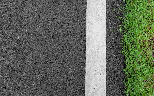 Strada grigio scuro scuro della strada del nero dell'asfalto ruvido di lerciume ed erba verde