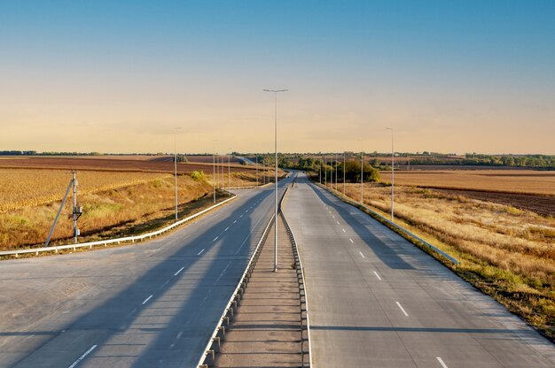 Strada in cemento con traffico a doppio senso, strisce divisorie, illuminazione, si allontana. Pista ad alta velocità, campi agricoli ai lati.