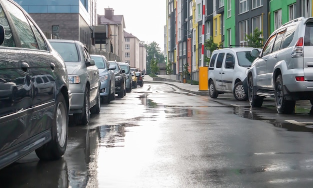 Strada in una città senza persone con auto parcheggiate in caso di pioggia. Pioggia sulla strada. Pioggia e auto. Sfondo di auto parcheggiate su una strada piovosa della città. Auto parcheggiate simmetriche.