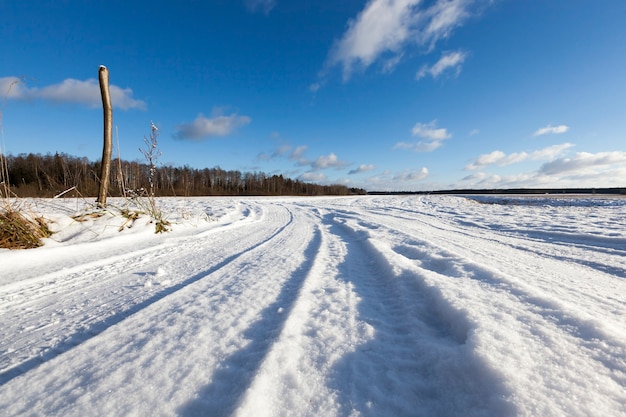 Strada innevata nella stagione invernale. Tracce visibili dell'auto. Cielo con nuvole sullo sfondo. A sinistra c'è un pezzo di un albero spezzato: il tronco