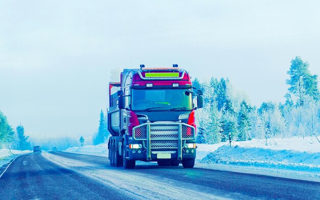 Strada invernale con neve. Camion in Finlandia. Autocarro e freddo paesaggio della Lapponia. Foresta d'Europa. Giro in autostrada della città finlandese. Carreggiata e percorso innevato viaggio su strada. Consegna in discesa carrabile