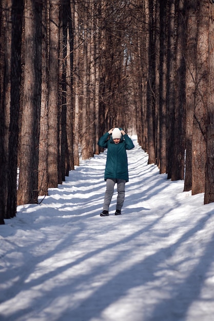 Strada rurale invernale giovane donna in abiti caldi cammina attraverso la foresta innevata nella soleggiata mattina d'inverno