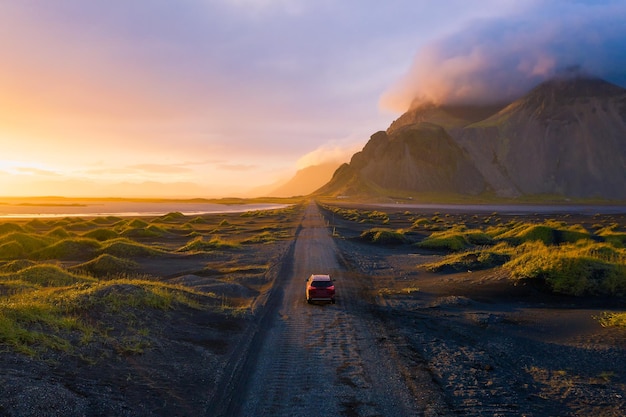 Strada sterrata al tramonto con il monte Vestrahorn e un'auto che guida l'Islanda