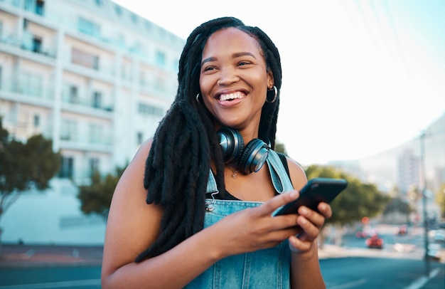 Strada studentesca e ragazza felice con smartphone che si gode una pausa per il tempo libero nel fine settimana a Los Angeles Hipster donna nera con sorriso in viaggio con telefono e cuffie per lo streaming musicale in città