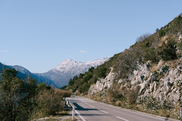 Strada tortuosa di montagna con un'auto che guida nella direzione opposta con vista sulle montagne e