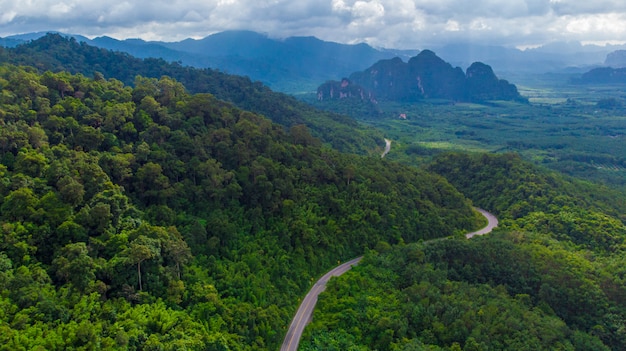 Strada tortuosa nella valle di montagna al tramonto. Vista aerea della strada asfaltata in Tailandia. Vista dall'alto della carreggiata, montagne, foresta verde, cielo blu e luce solare