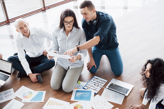 Strategia di pianificazione insieme. Squadra di affari che esamina i documenti sul pavimento con il responsabile che indica un'idea. Cooperazione aziendale. Disegnare il disegno di pianificazione. Concetto di lavoro di squadra