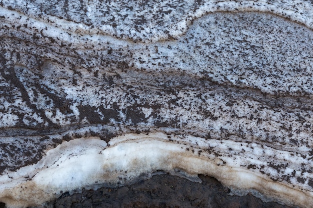 Strati di neve primaverile sporchi naturali sopra la struttura del primo piano del fango alla luce del giorno