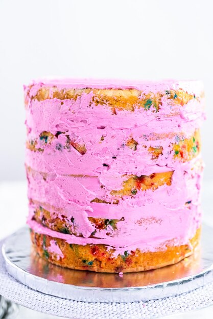 Strati di torta Funfetti con glassa di crema al burro rosa.