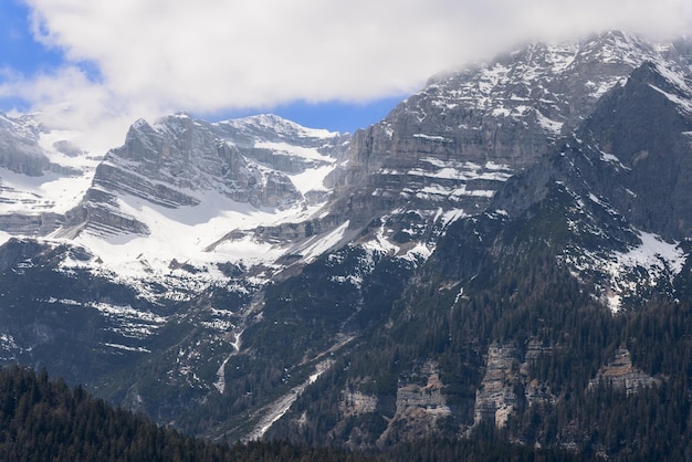 Strati rocciosi montuosi superbamente visibili di cime alpine ricoperte di foresta verde scuro e neve.