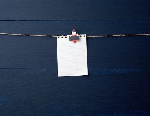 Strato di carta bianco vuoto del taccuino che appende sulla molletta da bucato decorativa di festa