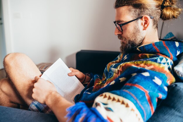 Strato di seduta barbuto del libro di lettura del giovane a casa