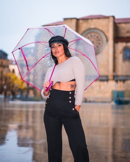 Street Style di una giovane mora latina sotto la pioggia della città con un ombrello trasparente