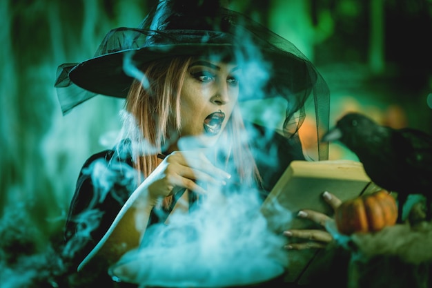 Strega con una faccia terribilmente in un ambiente inquietante e una ricetta di lettura di sfondo verde fumoso di bevanda magica manda il male. Concetto di Halloween.