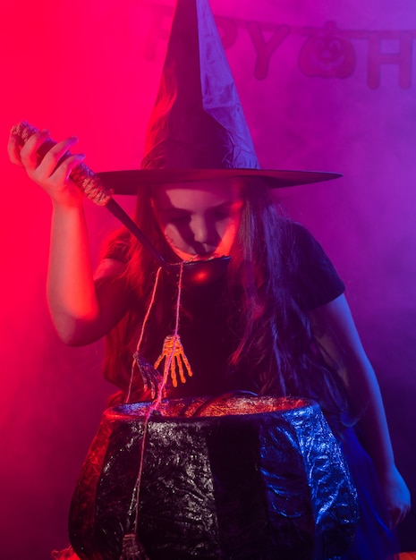 Strega della ragazza del bambino che prepara una pozione nel calderone alle feste di halloween